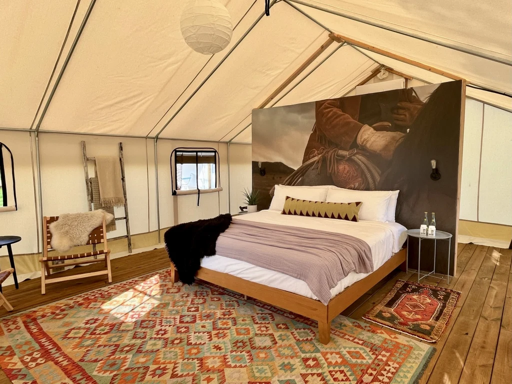 Spacious safari tent interior with queen bed, mini fridge, string lights, and air conditioning at Rancho Moonrise