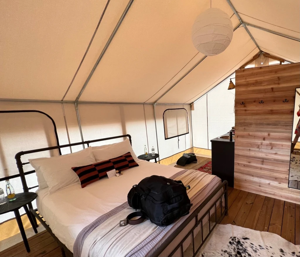Safari tent interior with cedar wall and black-frame bed at Rancho Moonrise