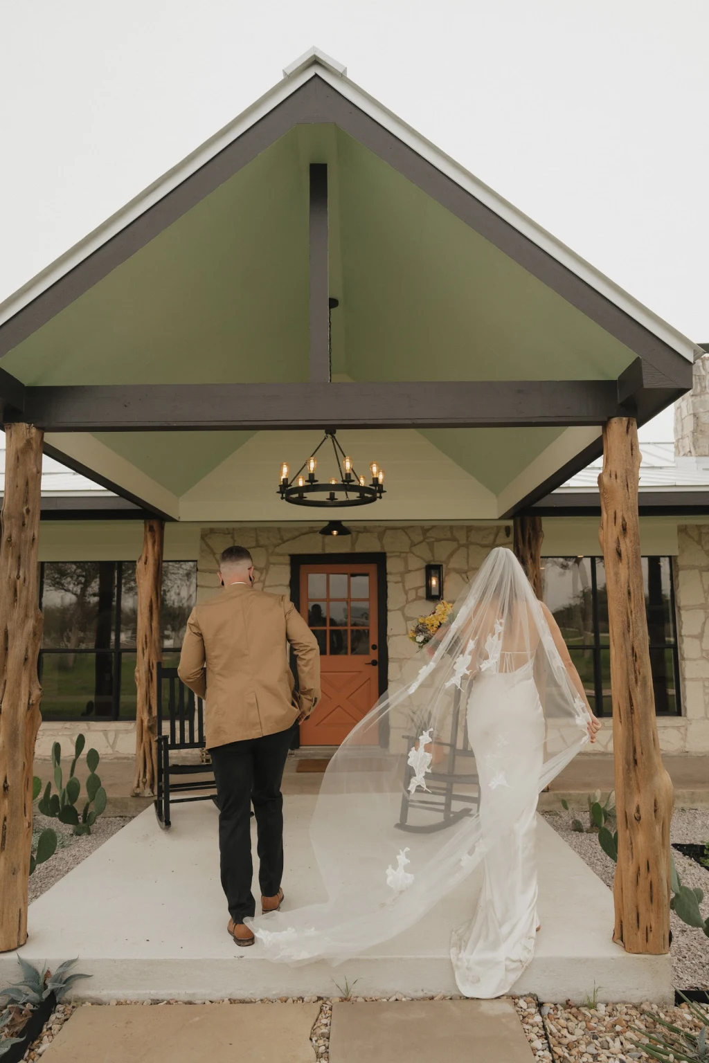 Bride and groom walking up to the Lodge porch with trailing veil at Rancho Moonrise